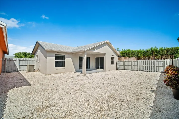 Exterior view featuring a covered patio, neutral-toned stucco siding, a gravel-surfaced yard, and privacy fencing