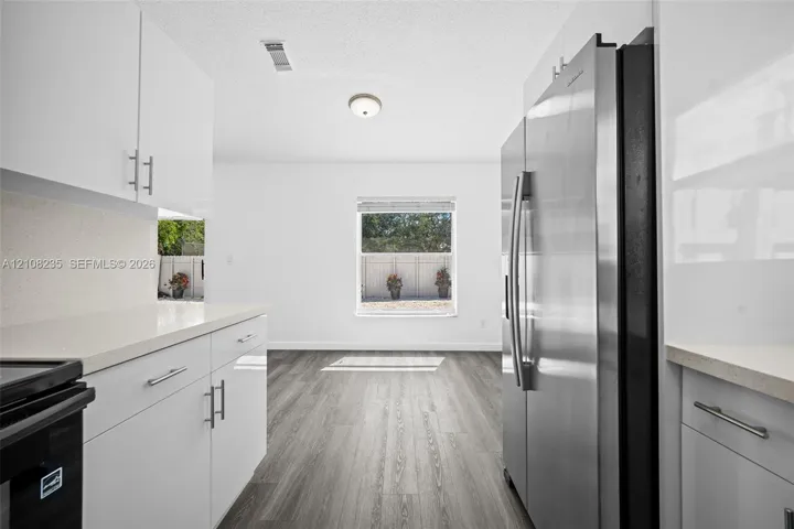 Kitchen featuring white flat-panel cabinetry, light-toned stone-surface countertops, wood-finish flooring, and a stainless steel side-by-side refrigerator