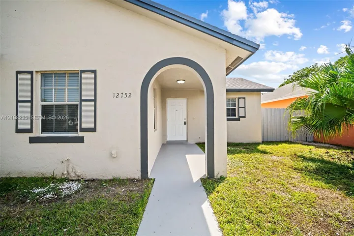 Stucco exterior featuring a covered arched entryway, grey-trimmed window shutters, a concrete walkway, and a hip roof