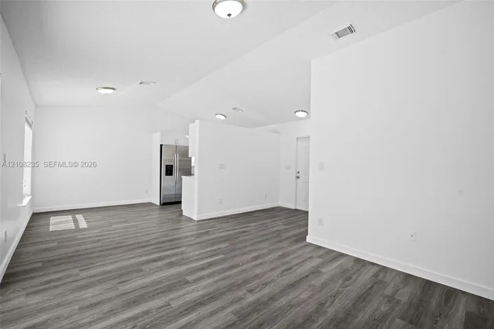 Vaulted ceiling with flush-mount lighting and wood-finish flooring throughout the open-concept space, featuring a stainless steel side-by-side refrigerator