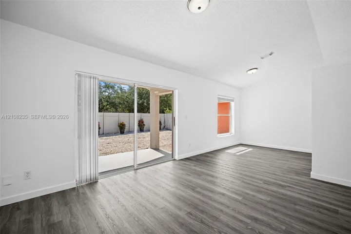 Interior space featuring wood-finish flooring, white walls, flush-mount ceiling lighting, a single-pane window, and glass sliding doors providing access to a covered concrete patio
