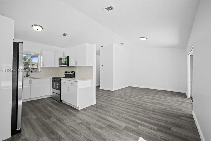 Kitchen featuring white cabinetry, solid-surface countertops, stainless steel appliances, and wood-finish flooring