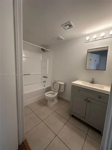 Spacious bathroom featuring ceramic tile flooring, a vanity with cabinet storage and integrated sink, a toilet, and a bathtub/shower combination with surround enclosure