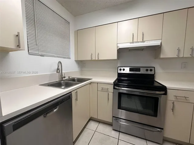 Kitchen featuring neutral flat-panel cabinetry, solid surface countertops, stainless steel appliances, a dual-basin sink with a gooseneck faucet, and tiled flooring