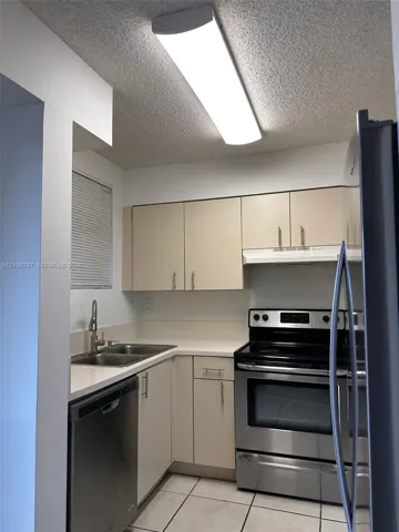 Kitchen featuring stainless steel appliances, double-basin sink with high-arc faucet, solid-surface countertops, flat-panel cabinetry, and tile flooring