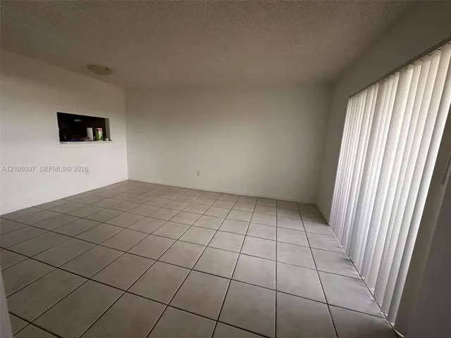 Room featuring neutral tile flooring, vertical window blinds, and a built-in wall pass-through