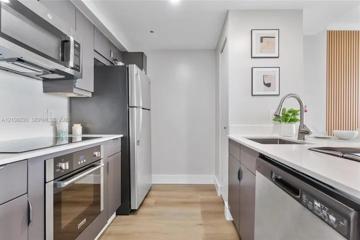 Kitchen featuring matte grey cabinetry, stainless steel appliances, light-toned stone countertops, and wood-finish flooring