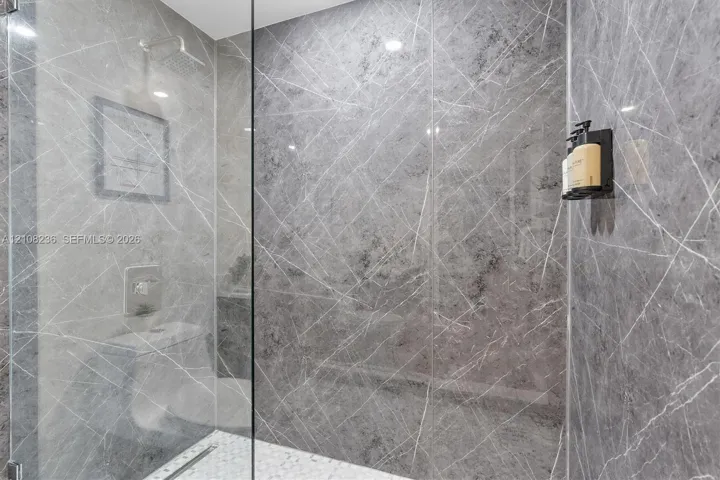 Walk-in shower featuring large-format grey veined tile wall surfacing, frameless glass enclosure, ceiling-mounted rainfall showerhead, and mosaic tile flooring
