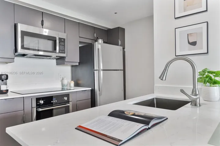 Kitchen featuring flat-panel cabinetry, quartz countertops, stainless steel appliances, and a gooseneck faucet with an undermount sink