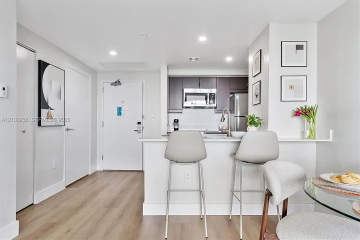 Kitchen featuring dark cabinetry, stainless steel microwave, wood-finish flooring, and a stone-surface breakfast bar with integrated sink