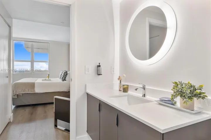 Bathroom vanity featuring a quartz countertop, integrated sink, matte dark cabinetry, and a circular LED-backlit mirror