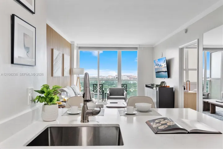 Kitchen featuring a white quartz countertop, undermount stainless steel sink, and high-arc faucet, accompanied by floor-to-ceiling windows and a private balcony