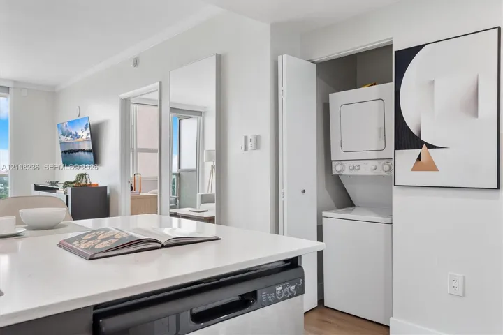 Kitchen featuring a white solid-surface countertop island, integrated stainless steel dishwasher, and stacked laundry unit housed in a bi-fold door closet