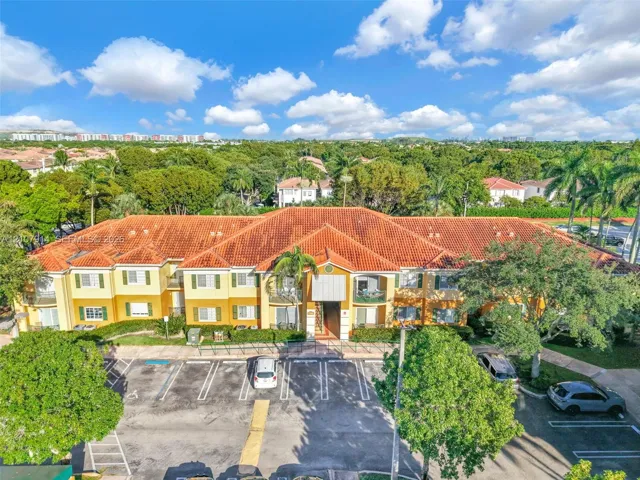 Low-rise multi-unit residential building featuring a barrel tile roof, stucco exterior, decorative shutters, and paved surface parking