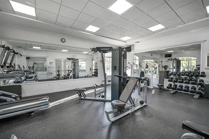 Fitness center featuring wall-to-wall mirrors, recessed grid ceiling lighting, and durable rubberized flooring