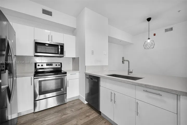 Kitchen featuring white cabinetry, solid surface countertops, stainless steel appliances, a single-basin undermount sink with a high-arch faucet, and wood-finish flooring