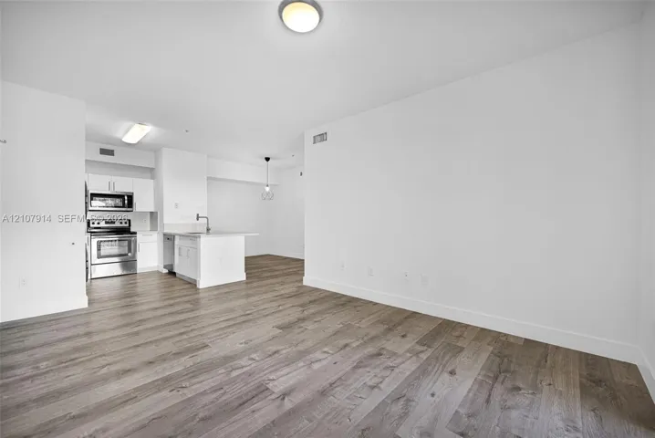 Open-concept interior featuring wood-finish flooring, white cabinetry, stainless steel appliances, and ceiling-mounted lighting fixtures