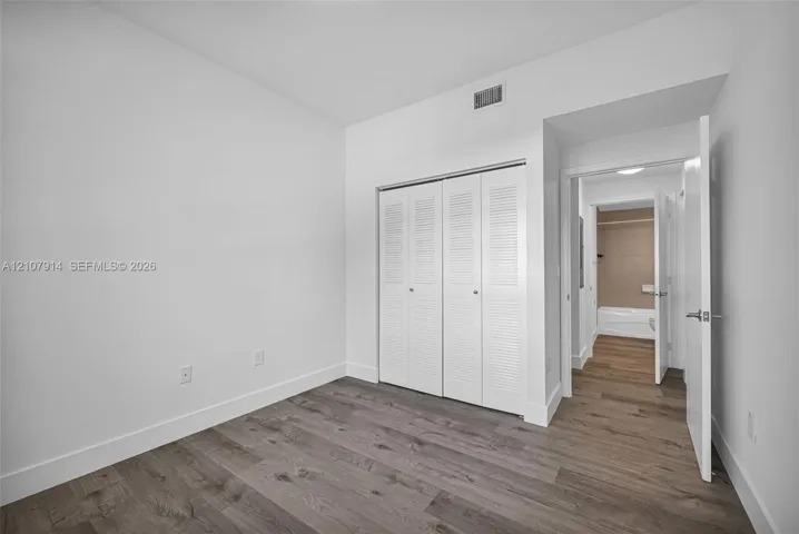 Room featuring wood-finish flooring, white walls, and a built-in double-door closet with louvered panels
