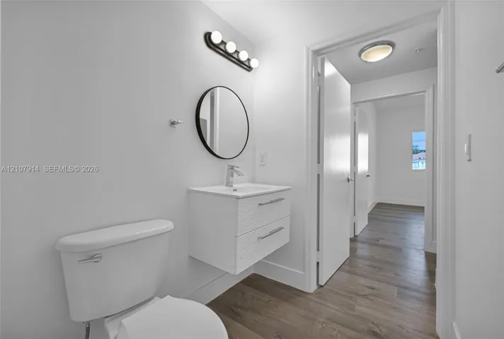 Floating white vanity with double drawers, round mirror, four-light matte black vanity fixture, and wood-finish flooring