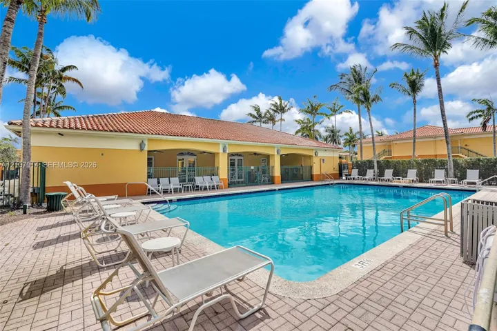 In-ground swimming pool featuring a concrete deck and a covered pavilion with arched entryways and a tile roof