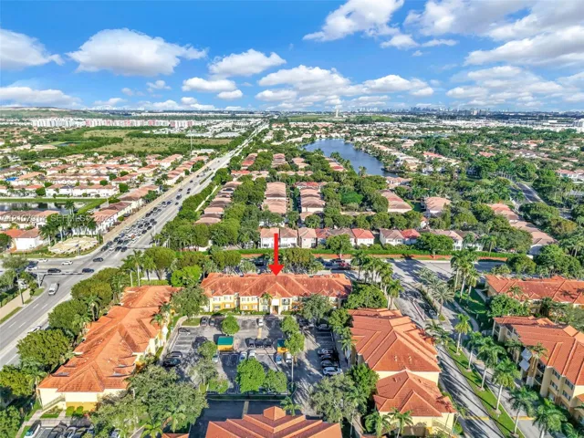 Aerial perspective of a multi-story residential building featuring terracotta tile roofing, stucco exterior, and a dedicated surface parking area surrounded by palm trees and mature landscaping