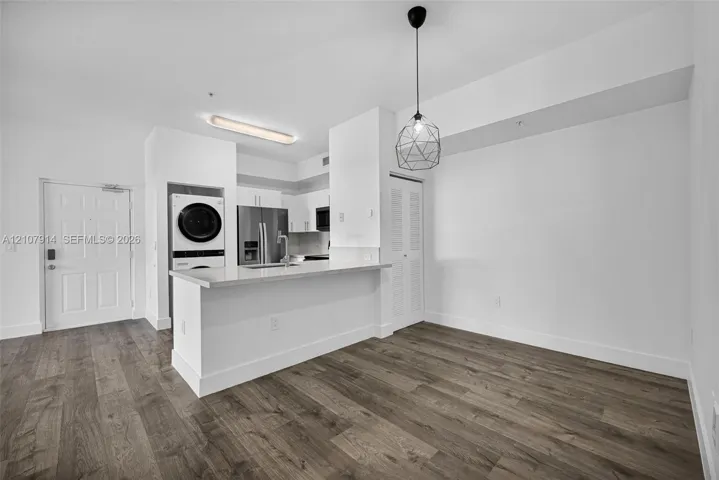 Kitchen featuring a breakfast bar with stone-surfaced countertop, stainless steel refrigerator, integrated laundry center, wood-finish flooring, and geometric pendant lighting