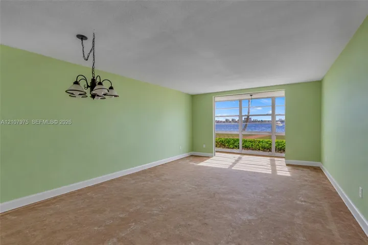 Spacious room featuring floor-to-ceiling windows with water exposure, wall-to-wall carpeting, and a multi-arm metal chandelier