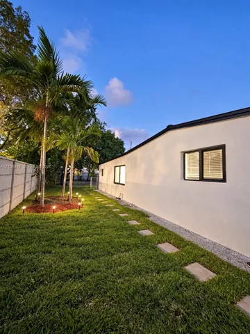 Side yard featuring a manicured lawn, established palm trees, a concrete block privacy wall, stone paver pathway, and recessed landscape lighting