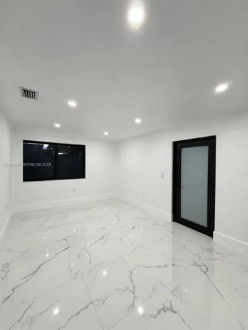 Polished large-format tile flooring with vein detailing, recessed ceiling lighting, and a modern door featuring a frosted glass panel and black frame