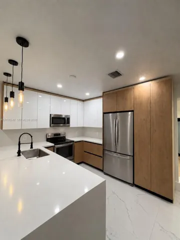 Kitchen featuring white gloss cabinetry, wood-finish lower cabinets, quartz countertops, stainless steel appliances, and matte black pendant lighting