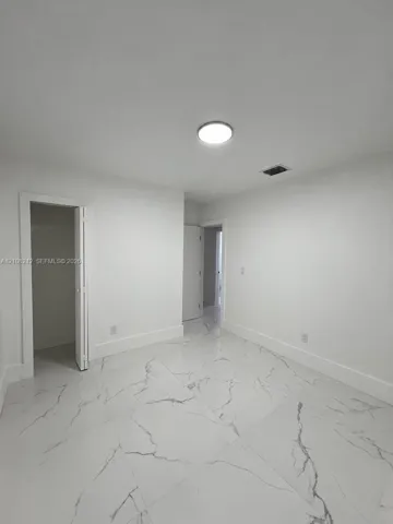 Neutral-toned interior space featuring large-format white stone-finish tile flooring with grey veining, a flush-mount circular ceiling light, and a built-in closet with bi-fold doors