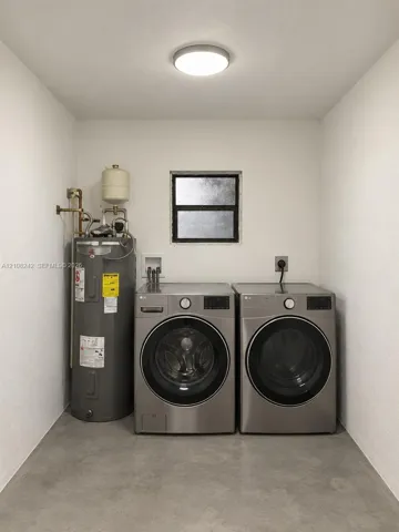 Utility space featuring a water heater, dual-stackable appliance connections, a single-hung window, and concrete flooring