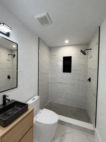 Walk-in shower featuring large-format tile surround, integrated recessed shelving, and a hexagonal tile floor