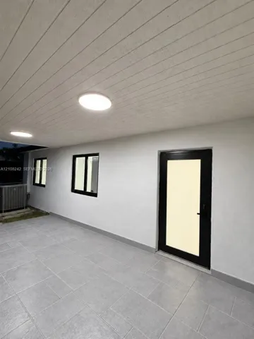 Covered outdoor patio featuring large-format grey tile flooring, tongue-and-groove ceiling paneling, recessed lighting, and a modern glass-panel door with a black frame