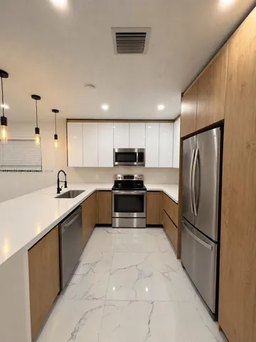 Kitchen featuring white gloss and wood-finish cabinetry, white solid-surface countertops, large-format veined tile flooring, stainless steel appliances, and matte black pendant lighting