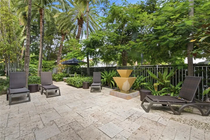Stone paver patio featuring a tiered fountain, metal perimeter fencing, and mature landscaping