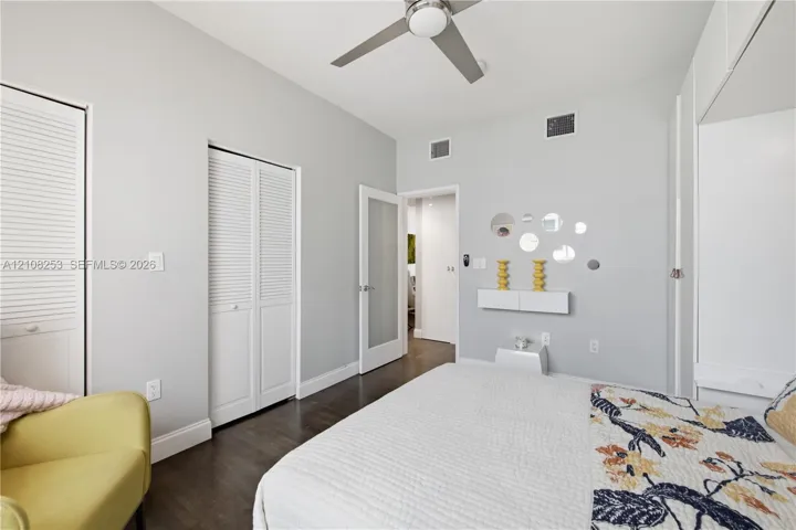 Wood-finish flooring, white louvered closet doors, modern ceiling fan with integrated lighting, and a white interior door with a frosted glass pane