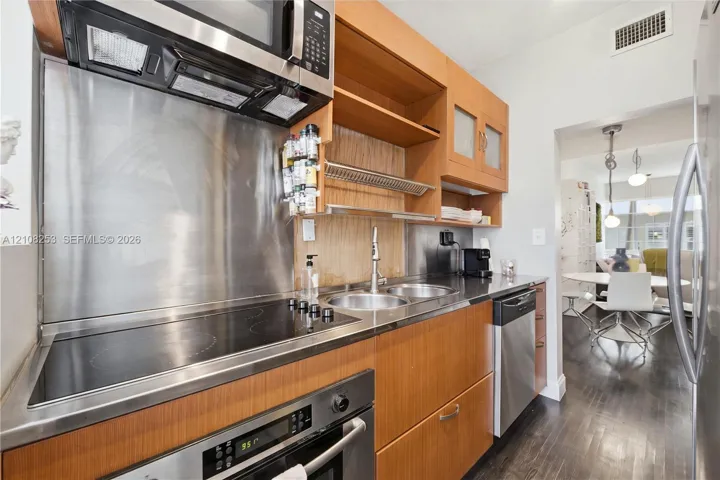 Kitchen featuring wood cabinetry, stainless steel appliances, electric cooktop, integrated stainless steel backsplash, and double-basin sink