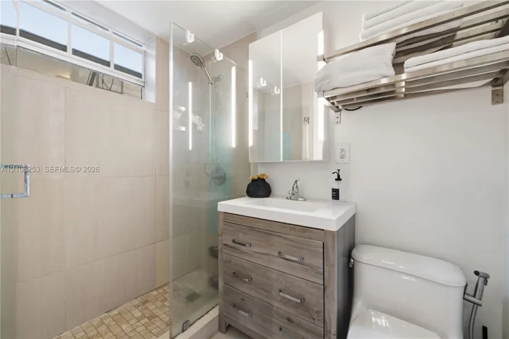 Walk-in shower featuring floor-to-ceiling tile, frameless glass enclosure, and a handheld shower head