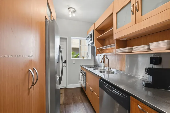 Galley kitchen featuring wood-finish cabinetry, stainless steel countertops, integrated stainless steel appliances, and wood-finish flooring