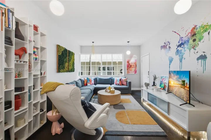 Floor-to-ceiling white built-in shelving, multi-pane window, integrated low-profile media cabinetry with under-cabinet lighting, and dark-finish flooring