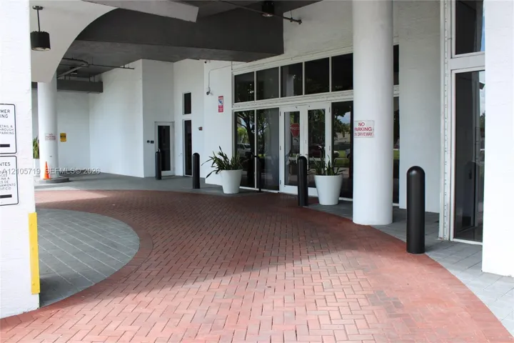 Covered drive-up entrance featuring a herringbone brick paver motor court, structural cylindrical columns, and expansive glass-paneled double entry doors