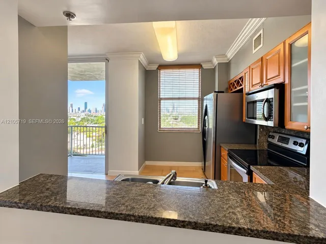Kitchen featuring a granite countertop peninsula, natural wood cabinetry with glass-front display panels, stainless steel built-in microwave, and crown molding