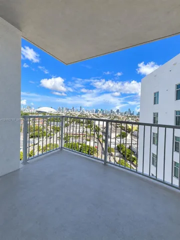 Covered balcony featuring concrete flooring and a metal railing, overlooking an urban skyline