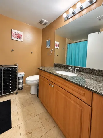 Bathroom featuring a wood-finish vanity with a stone-composite countertop, undermount sink, expansive wall-mounted mirror, and tile flooring