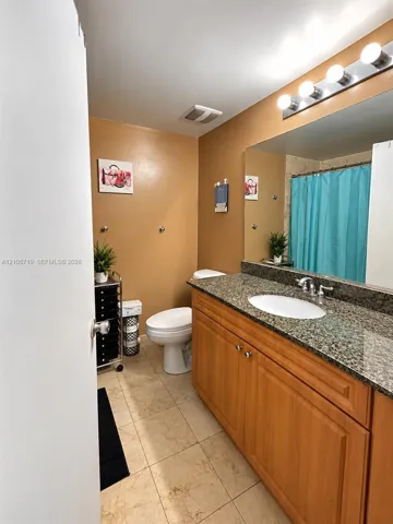 Bathroom featuring a wood-finish vanity with an integrated stone-patterned countertop, oval undermount sink, full-width wall mirror, and tiled flooring