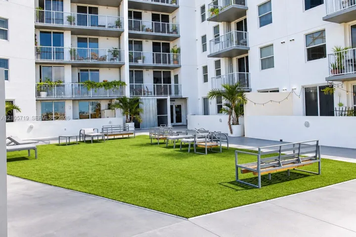 Outdoor courtyard featuring a manicured lawn, smooth concrete perimeter, perimeter wall lighting, and established palm trees