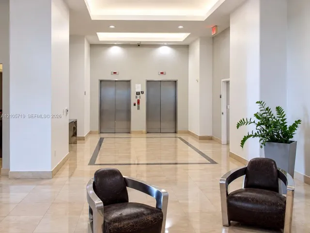 Lobby featuring polished stone flooring with a central inlay border, dual stainless steel elevator doors, and recessed tray ceiling lighting