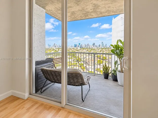 Private balcony featuring concrete flooring, a metal railing, and a cityscape backdrop, accessible through glass sliding doors