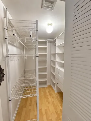 Walk-in closet featuring wood-finish flooring, built-in floor-to-ceiling shelving, integrated drawer units, and tiered metal wire racking